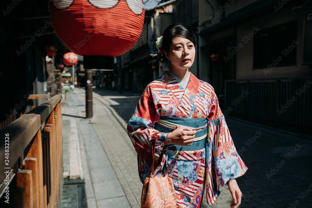 身着传统日本和服的女子平静地走过京都历史悠久的街道,街道上有传统的木制建筑和红灯笼
