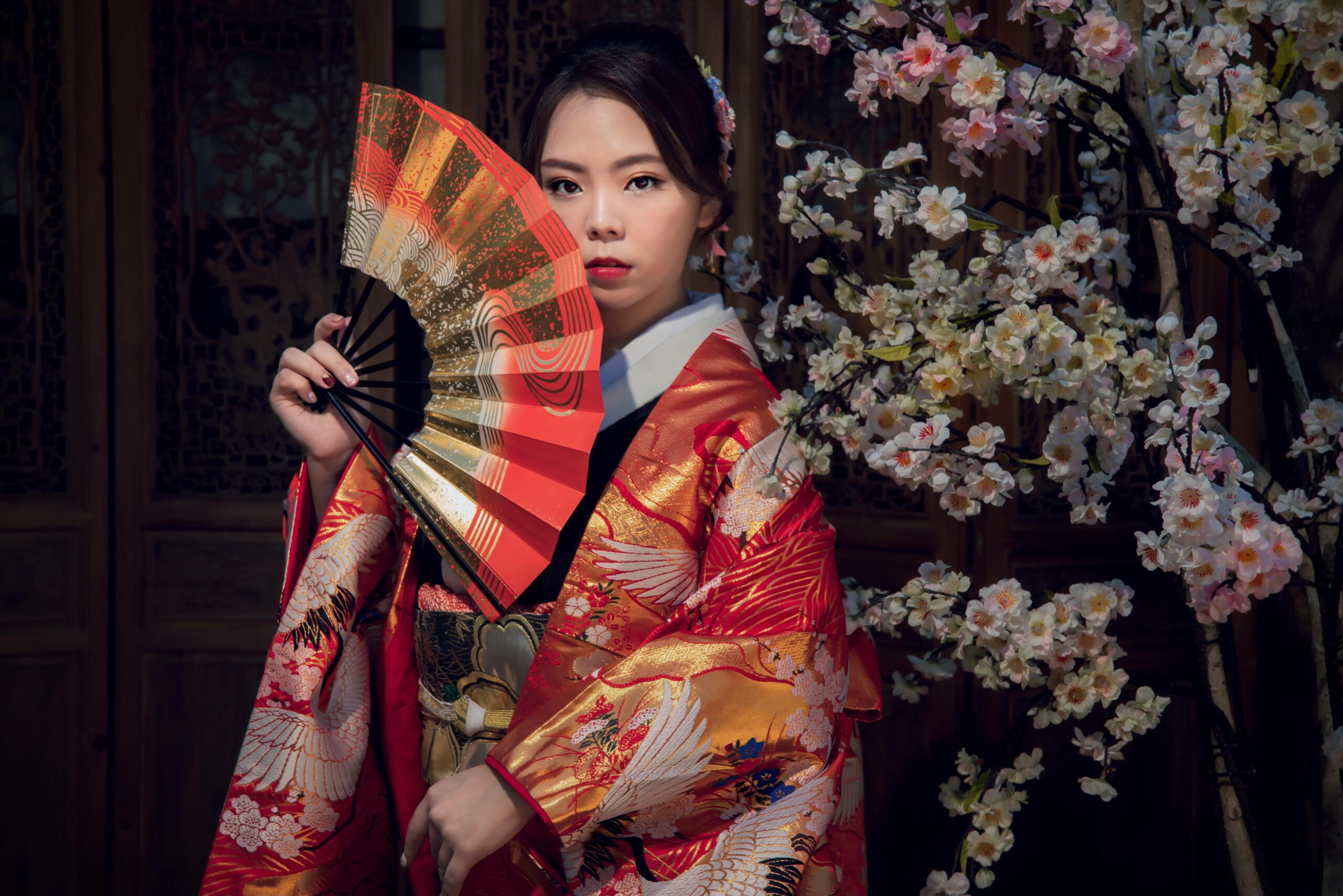 身着传统红色和服的女子优雅地手持装饰性日本扇子,以经典姿势展示传统的面罩摄影技术